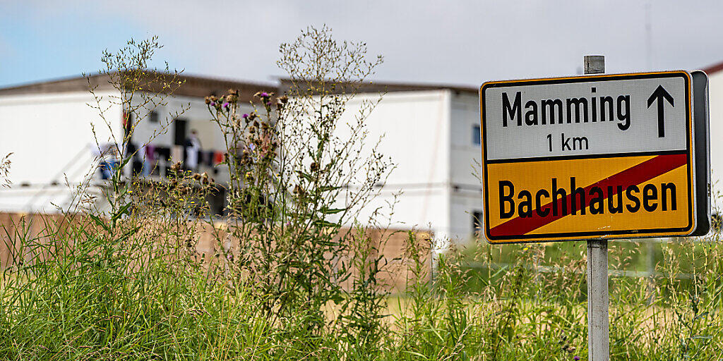 Das Ortsschild von Mamming, im Hintergrund sind die Unterkünfte von Erntehelfern zu sehen. Foto: Armin Weigel/dpa