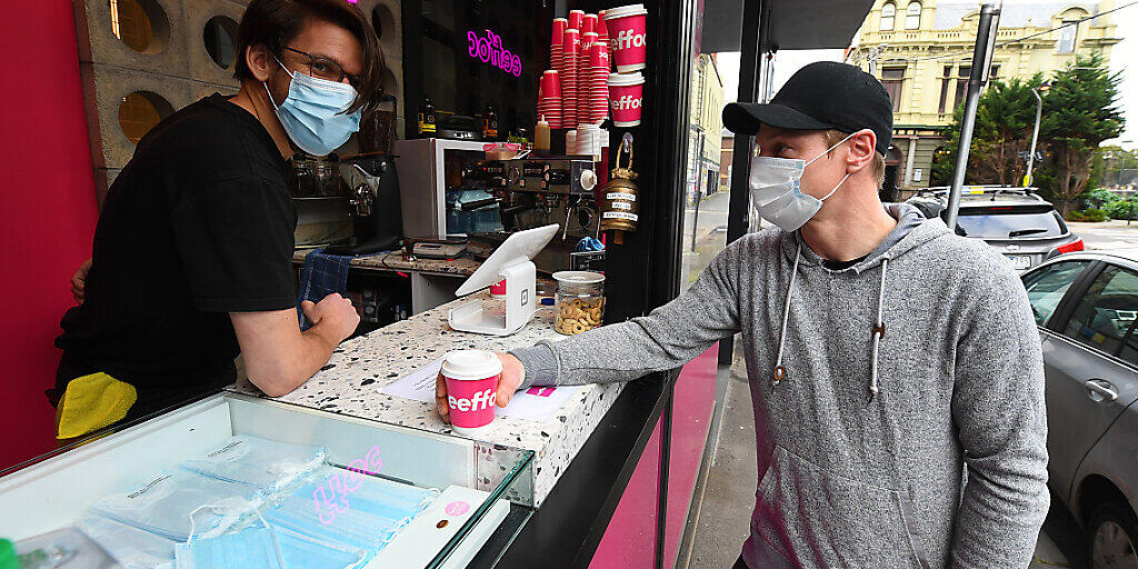 Barista Alex Pallas (left) serves a customer a coffee and facemask at Eeffoc Cafe in Prahran, Melbourne, Wednesday, July 22, 2020. Eeffoc Cafe in Prahran is handing out single use face masks with takeaway coffee purchase. (AAP Image/James Ross) NO ARCHIVING