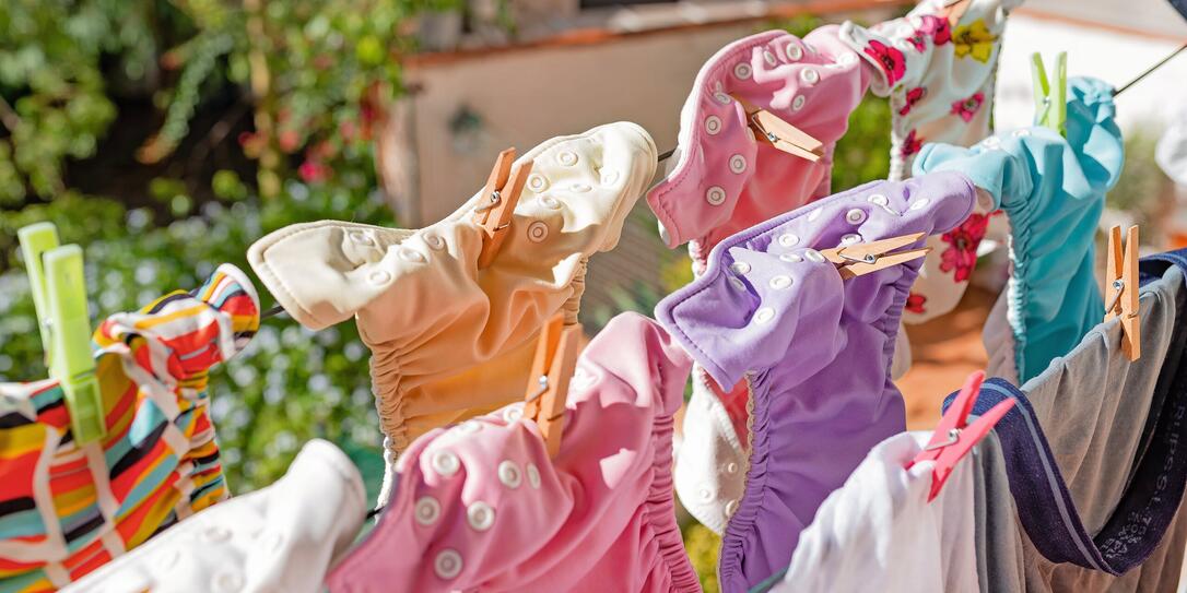 Cloth diapers hanging while drying under the sun on clothesline. Laundry of colorful reusable nappies for babies.