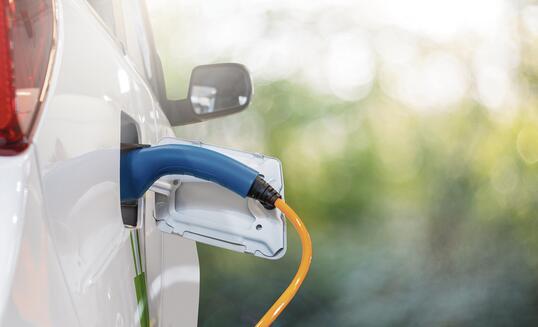 Close up of electric car inlet with a connected charging cable on a green background