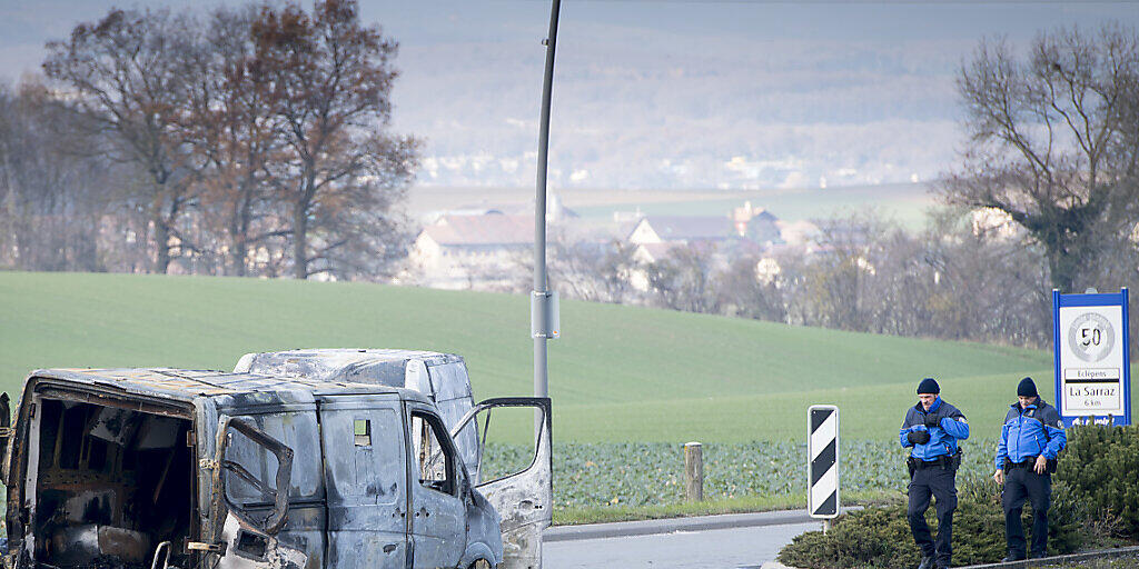 Polizisten begutachten am Tag nach dem Überfall den ausgebrannten Geldtransporter. (KEYSTONE/Laurent Gillieron)