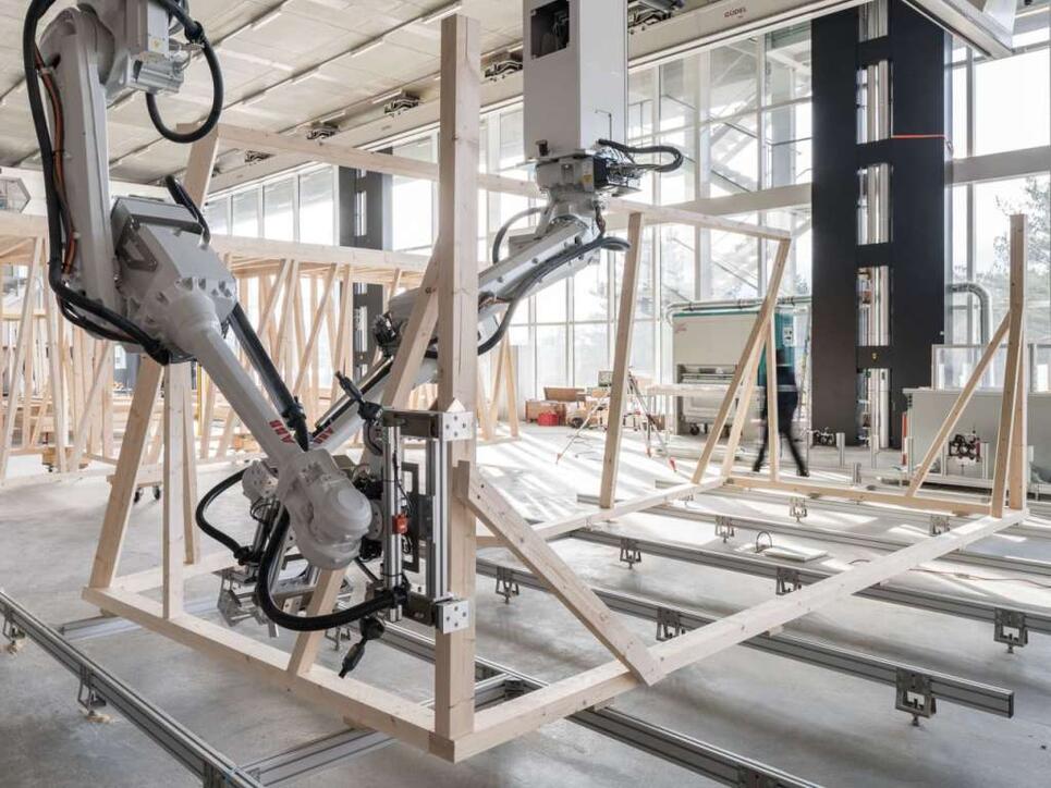 Zwei Roboter arbeiten beim Zusammenbau des Holzmoduls zusammen. Ihr Bewegungspfad wird laufend anhand des Baufortschritts berechnet.