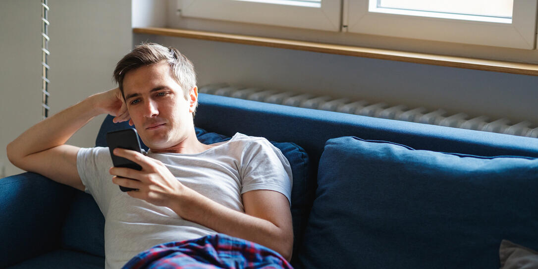 Young man on the sofa in pajamas checking smart phone