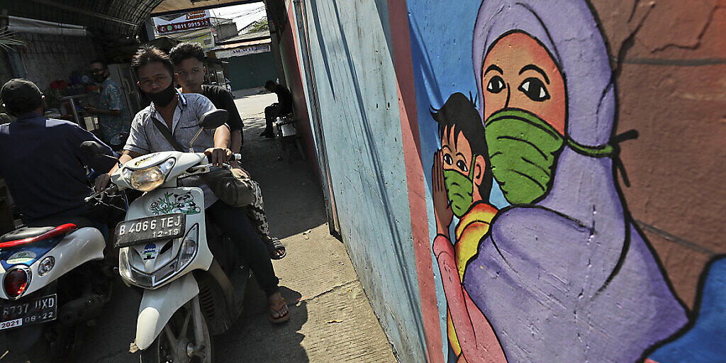 Ein Wandbild in Jakarta zeigt eine Frau und ein Kind, die Mundschutz tragen. Foto: Dita Alangkara/AP/dpa