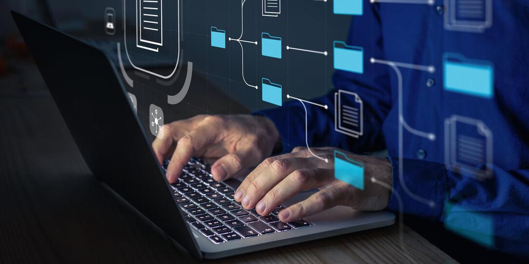 Document Management System (DMS) being setup by IT consultant working on laptop computer in office. Software for archiving, searching and managing corporate files and information. Business processes