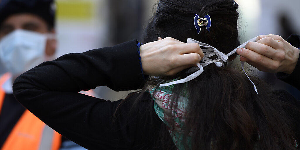 Eine Frau zieht eine Maske an vor dem Eingang zur Covid-19-Triage im Berner Inselspital. Quelle: KEYSTONE Fotograf: ANTHONY ANEX