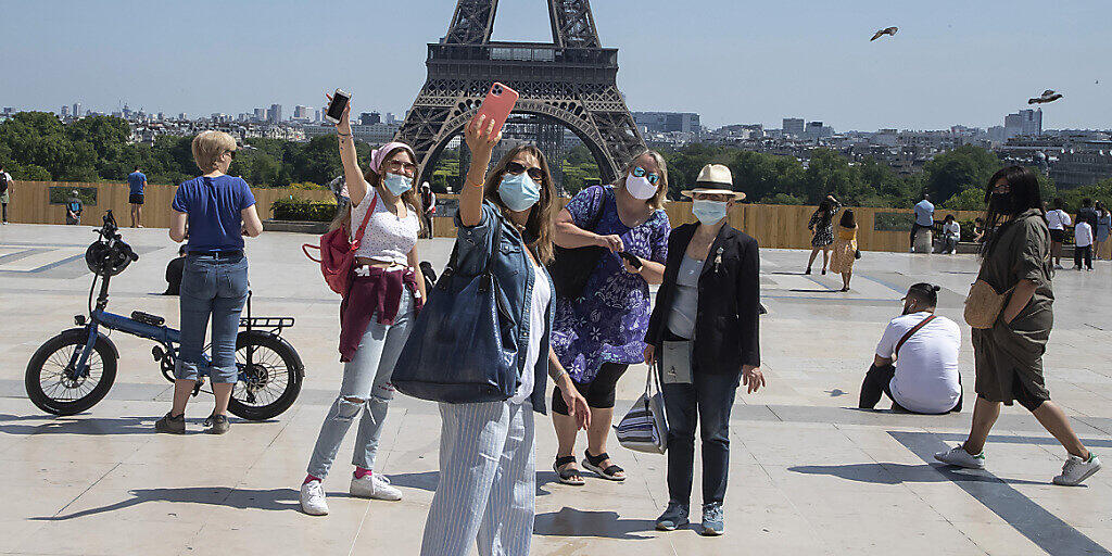 Menschen mit Mundschutzen machen Selfies vor dem Eiffelturm auf dem Trocadero-Platz. Die Pariser genießen ihr erstes Wochenende in der Sonne seit den teilweisen Lockerungen der Reise- und Bewegungsbeschränkungen. Foto: Michel Euler/AP/dpa
