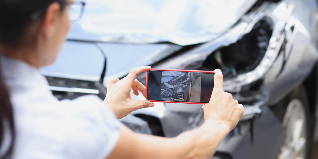 Insurance agent woman takes pictures by smartphone of car damage after road accident