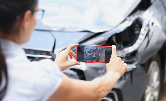 Insurance agent woman takes pictures by smartphone of car damage after road accident