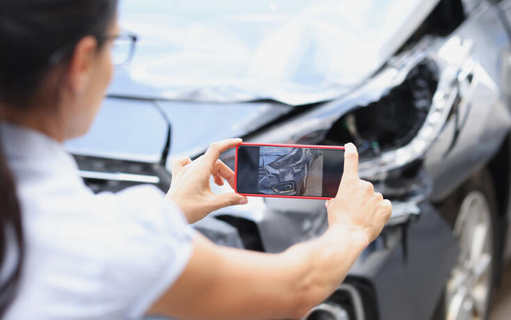 Insurance agent woman takes pictures by smartphone of car damage after road accident