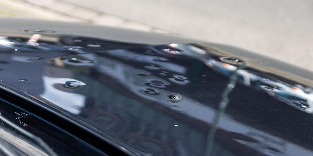 Car engine hood with many hail damage dents show the forces of nature and the importance of car insurance and a replacement value insurance against stormy weather and storm hazards or extreme weather