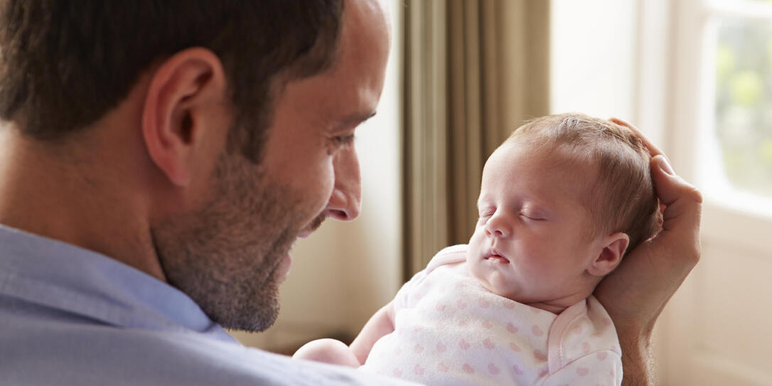 Father At Home With Sleeping Newborn Baby Daughter